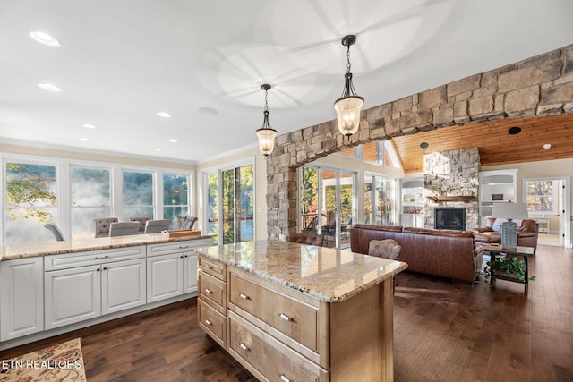 kitchen featuring a stone fireplace, light stone countertops, pendant lighting, open floor plan, and dark wood-style flooring