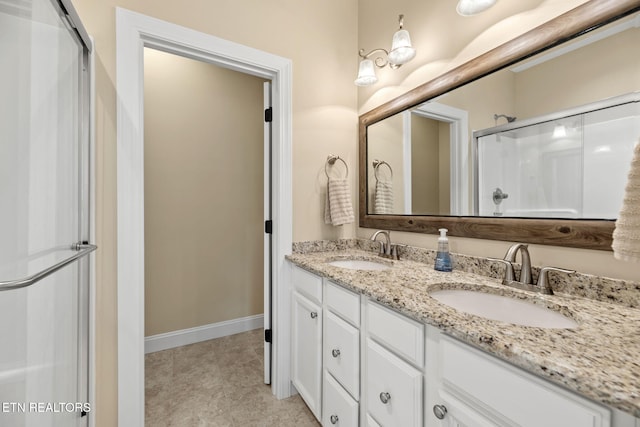 bathroom with baseboards, a sink, double vanity, and a stall shower