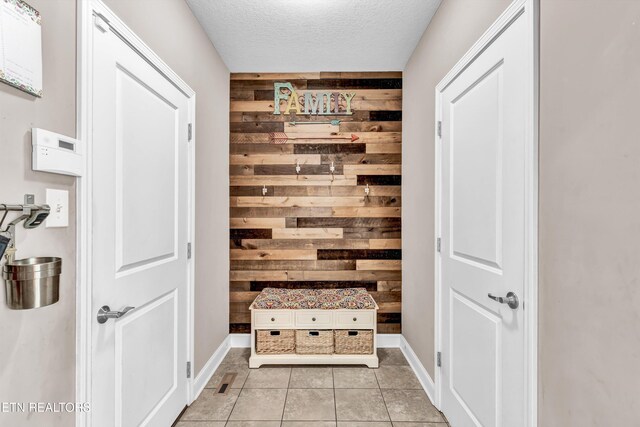 mudroom with wood walls, a textured ceiling, baseboards, and light tile patterned flooring