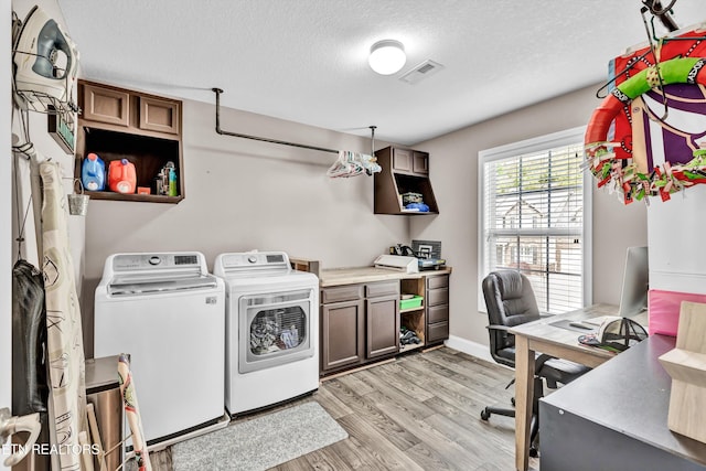 laundry room with a textured ceiling, visible vents, light wood-style floors, washer and clothes dryer, and cabinet space