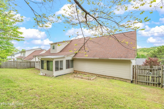 back of house with a sunroom, a fenced backyard, roof with shingles, and a yard