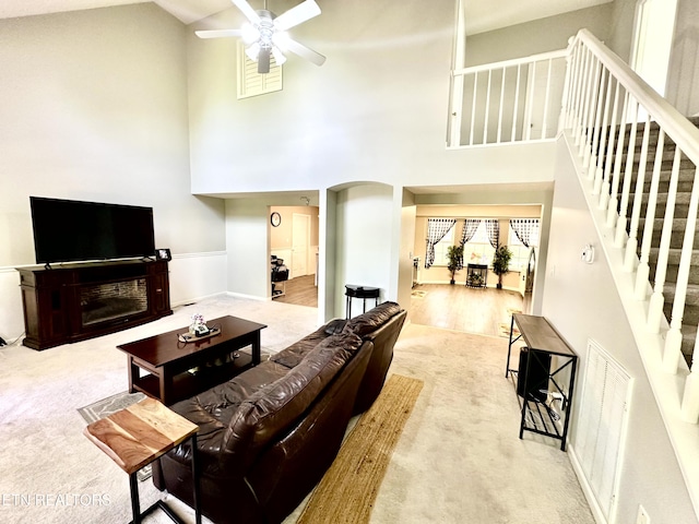 living area featuring visible vents, stairs, ceiling fan, high vaulted ceiling, and carpet flooring