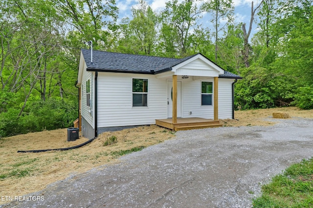 bungalow-style house with driveway, roof with shingles, and central AC unit