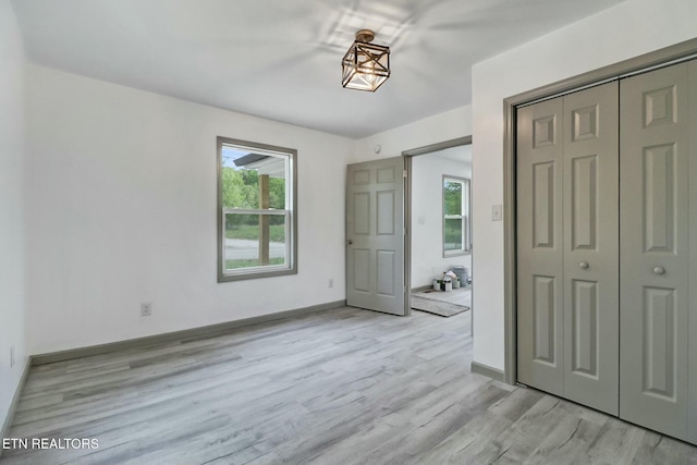 unfurnished bedroom featuring baseboards, light wood-style floors, a closet, and multiple windows