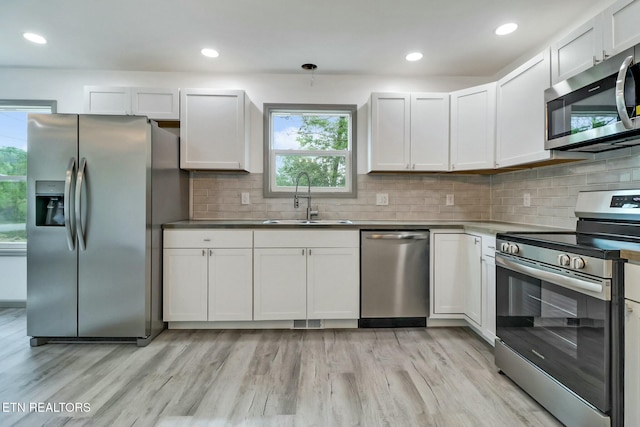 kitchen with appliances with stainless steel finishes, tasteful backsplash, a sink, and light wood finished floors