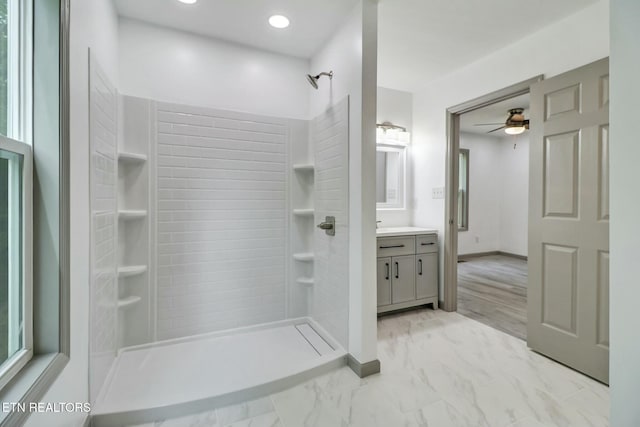 full bath with a tile shower, marble finish floor, a ceiling fan, vanity, and baseboards