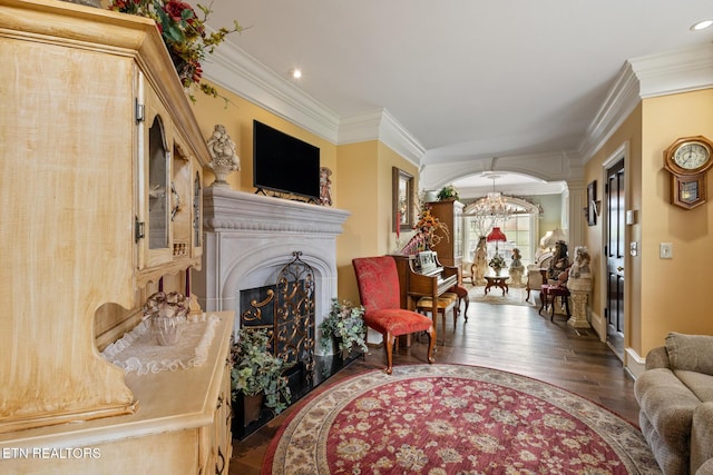 living room featuring a fireplace with raised hearth, a chandelier, ornamental molding, and wood finished floors