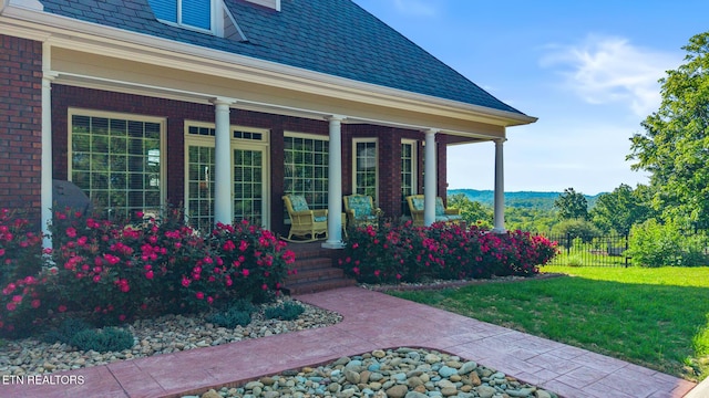 entrance to property with fence, a yard, a porch, and brick siding