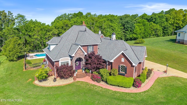 english style home with stone siding, an outdoor pool, a front yard, and a chimney