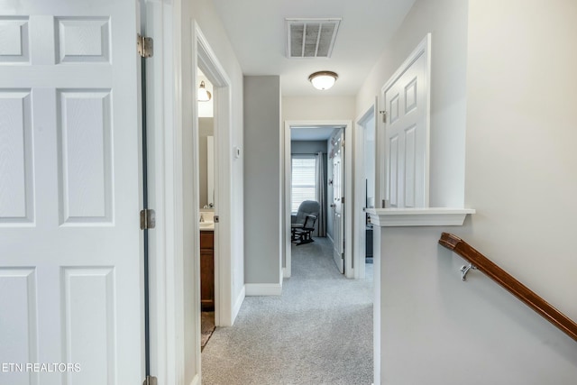 hall with an upstairs landing, light colored carpet, visible vents, and baseboards
