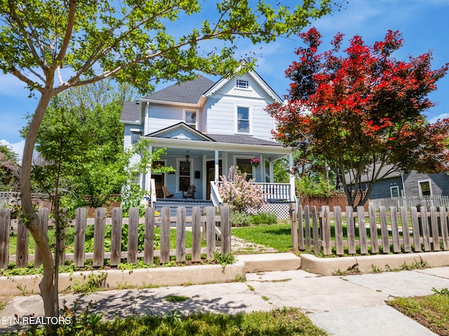 victorian-style house featuring a porch, a shingled roof, and a fenced front yard