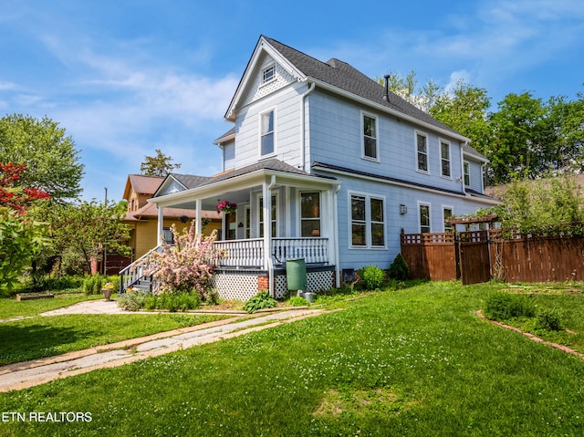 view of front of home with a front yard, a shingled roof, covered porch, and fence