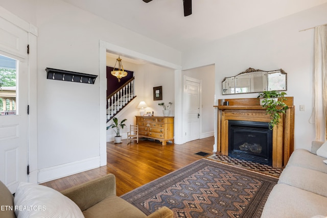 living area featuring stairway, a fireplace with flush hearth, ceiling fan, baseboards, and wood finished floors