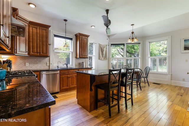 kitchen with stainless steel dishwasher, a healthy amount of sunlight, a kitchen island, light wood finished floors, and backsplash