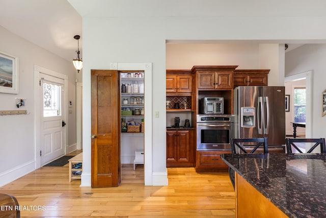 kitchen with dark stone counters, pendant lighting, stainless steel appliances, and light wood-style floors