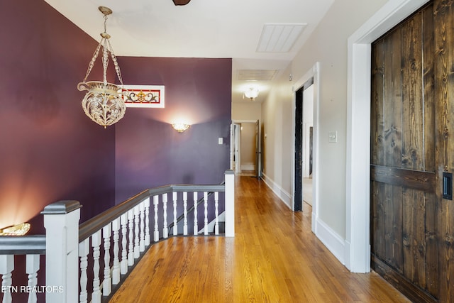 hallway featuring baseboards, visible vents, wood finished floors, and an upstairs landing