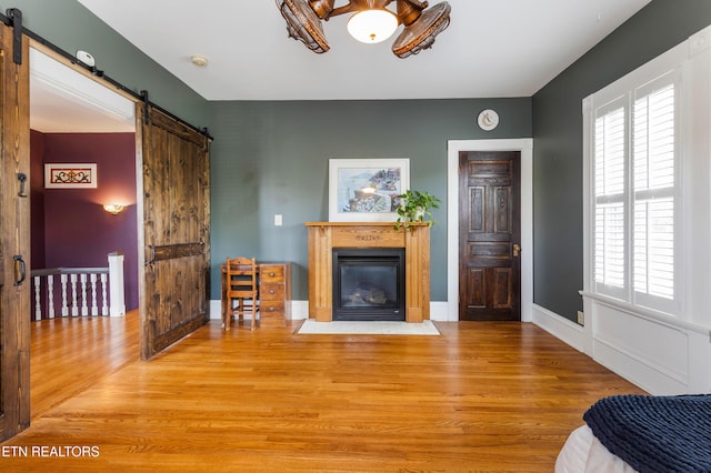 living area with baseboards, a barn door, a fireplace with flush hearth, and light wood finished floors