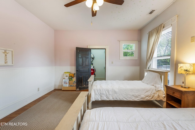 bedroom featuring visible vents, wood finished floors, a wainscoted wall, and ceiling fan