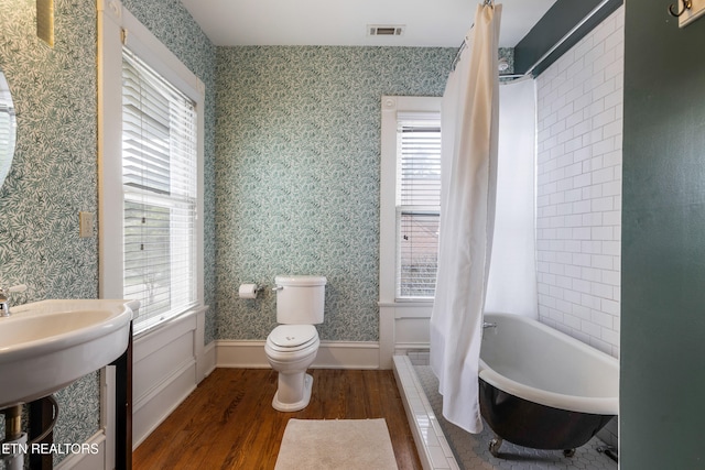 full bathroom with a wealth of natural light, toilet, visible vents, wallpapered walls, and wood finished floors