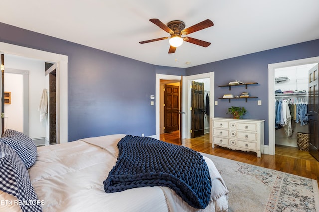 bedroom featuring wood finished floors, a closet, ceiling fan, baseboards, and a spacious closet
