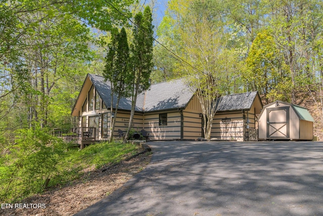 view of front facade with a storage unit, a garage, a shingled roof, a deck, and an outdoor structure