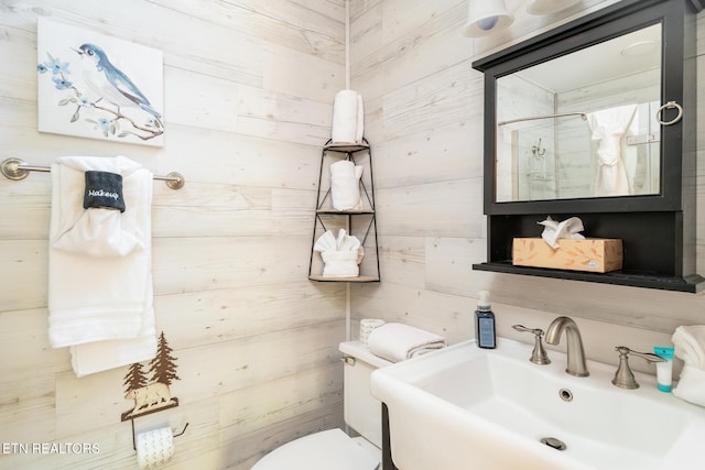 bathroom featuring toilet, walk in shower, wood walls, and a sink