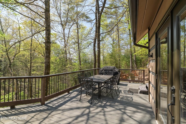 deck with outdoor dining area and a wooded view