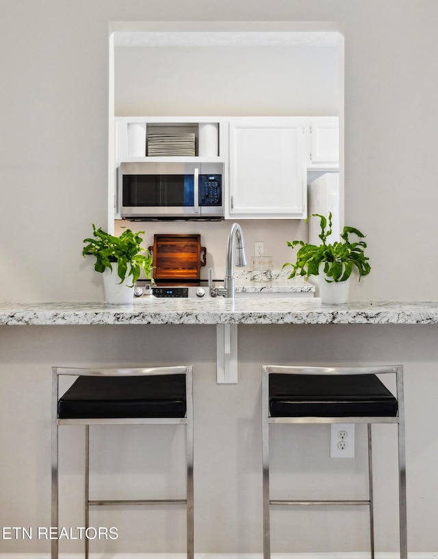 kitchen with stainless steel microwave, light stone counters, a sink, and white cabinets