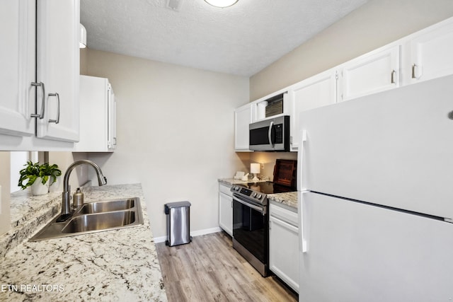 kitchen with light wood finished floors, a sink, baseboards, appliances with stainless steel finishes, and white cabinetry
