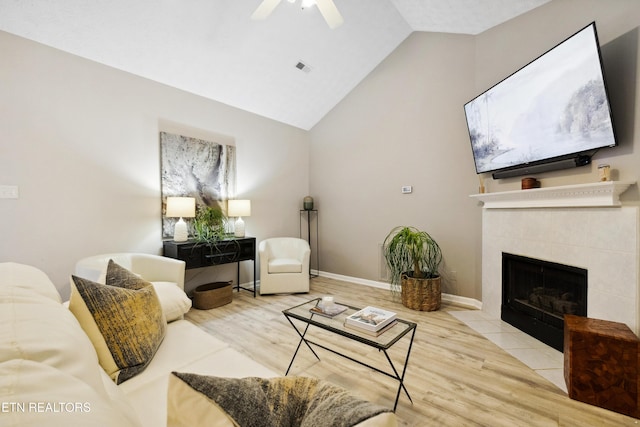 living area with vaulted ceiling, wood finished floors, a ceiling fan, baseboards, and a tiled fireplace