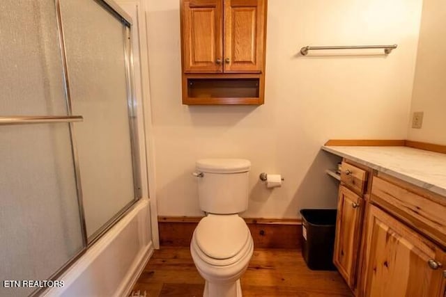 bathroom featuring shower / bath combination with glass door, wood finished floors, toilet, and baseboards