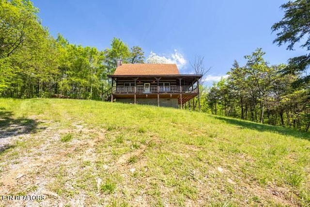 rear view of property with a wooden deck, a chimney, and a view of trees