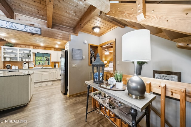 kitchen featuring freestanding refrigerator, light wood-type flooring, dark stone counters, white cabinets, and a sink