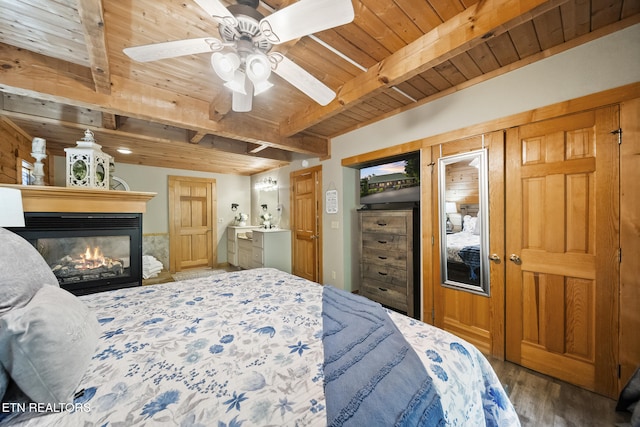 bedroom with beam ceiling, a glass covered fireplace, wood ceiling, and wood finished floors