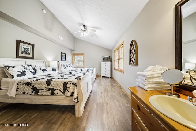 bedroom with wood finished floors, lofted ceiling, baseboards, a textured ceiling, and a sink