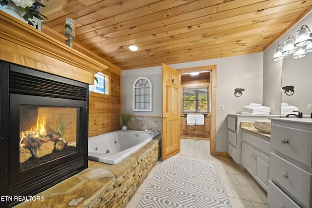 full bath with tile patterned flooring, vanity, a multi sided fireplace, a tub with jets, and wood ceiling