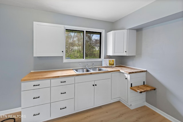 kitchen with white cabinets, wooden counters, a sink, light wood-style floors, and baseboards