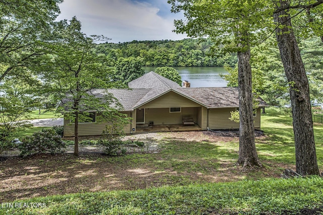 exterior space featuring a chimney, a front yard, a wooded view, a water view, and a shingled roof