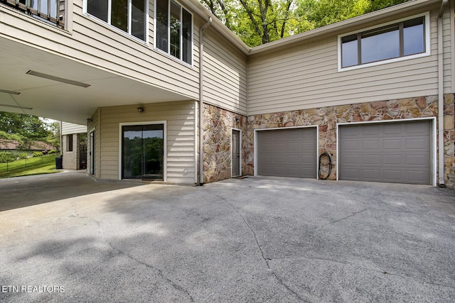 view of side of property featuring an attached garage, driveway, and stone siding