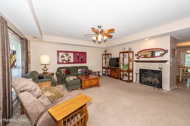 living room with a fireplace, light colored carpet, a ceiling fan, and a tray ceiling