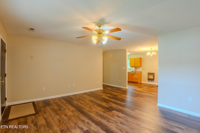 unfurnished room featuring visible vents, dark wood-style floors, baseboards, heating unit, and ceiling fan with notable chandelier