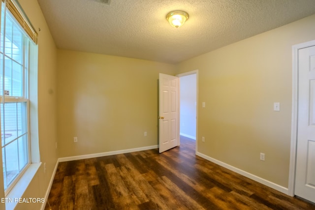 empty room with a textured ceiling, dark wood finished floors, and baseboards
