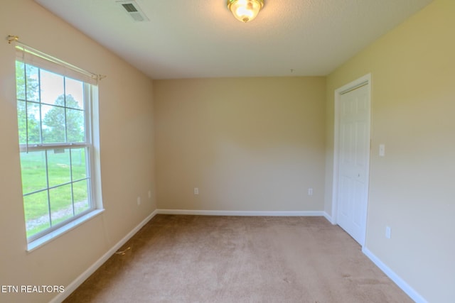 unfurnished room featuring visible vents, baseboards, light colored carpet, and plenty of natural light