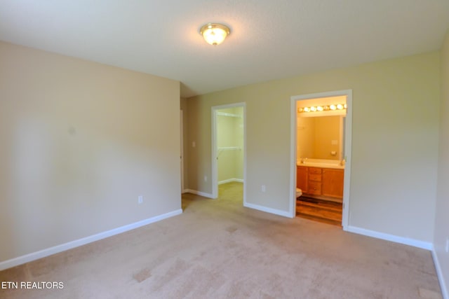 unfurnished bedroom featuring connected bathroom, light colored carpet, a closet, baseboards, and a spacious closet