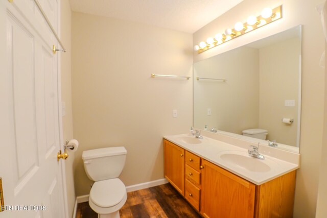 bathroom featuring wood finished floors, double vanity, toilet, a sink, and baseboards