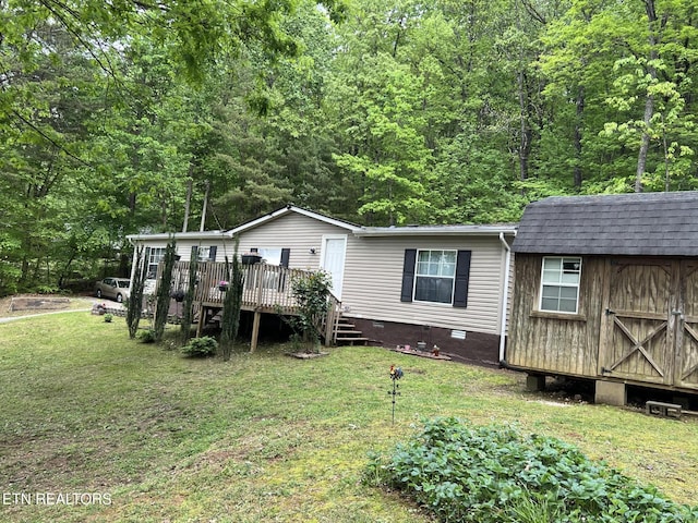 rear view of property featuring a wooden deck, a shed, crawl space, a lawn, and an outbuilding