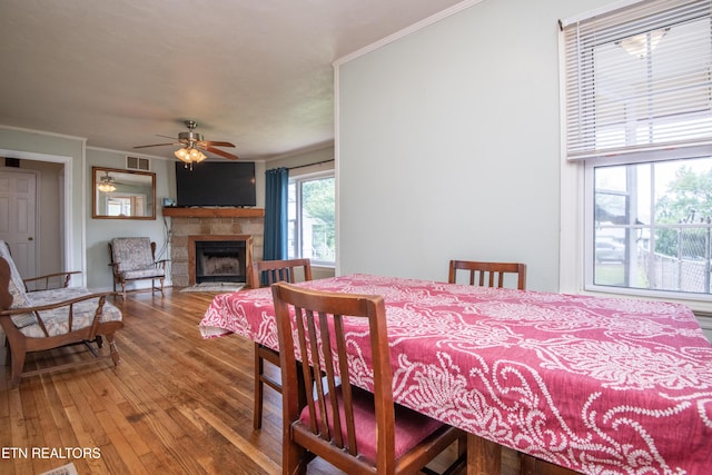dining area featuring crown molding, a ceiling fan, visible vents, wood finished floors, and a fireplace with flush hearth
