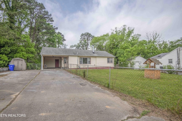 view of front facade featuring a storage shed, a front yard, a carport, fence private yard, and driveway