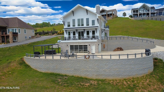back of property with board and batten siding, an attached garage, a chimney, and a lawn