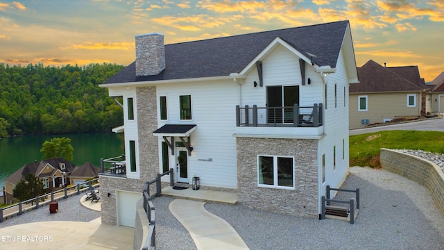 view of front of home with a chimney, a balcony, concrete driveway, stone siding, and a garage
